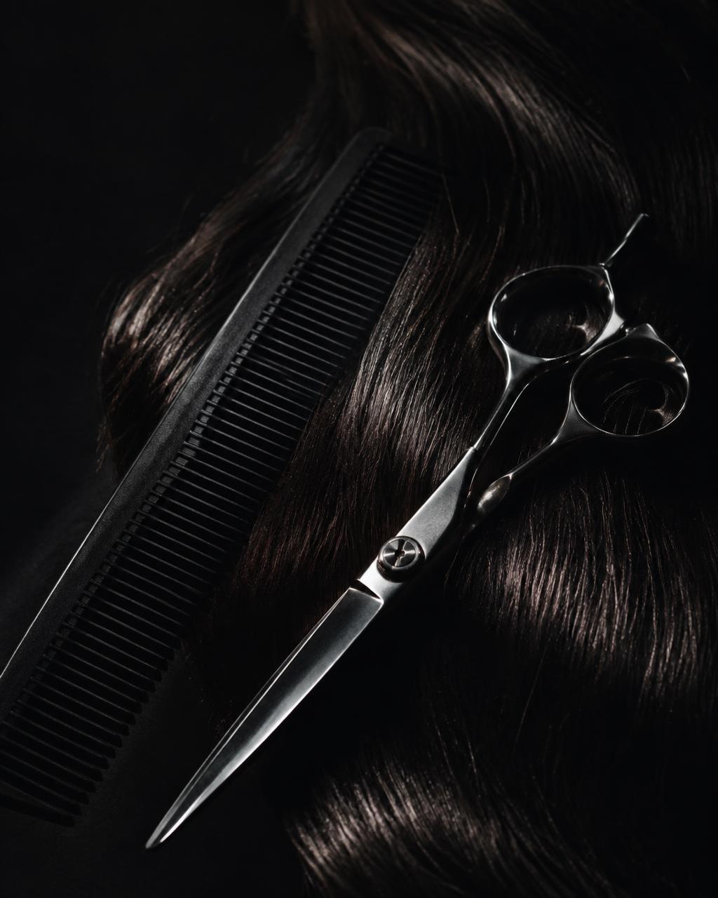 A cutting comb and steel shears resting on dark glossy hair
